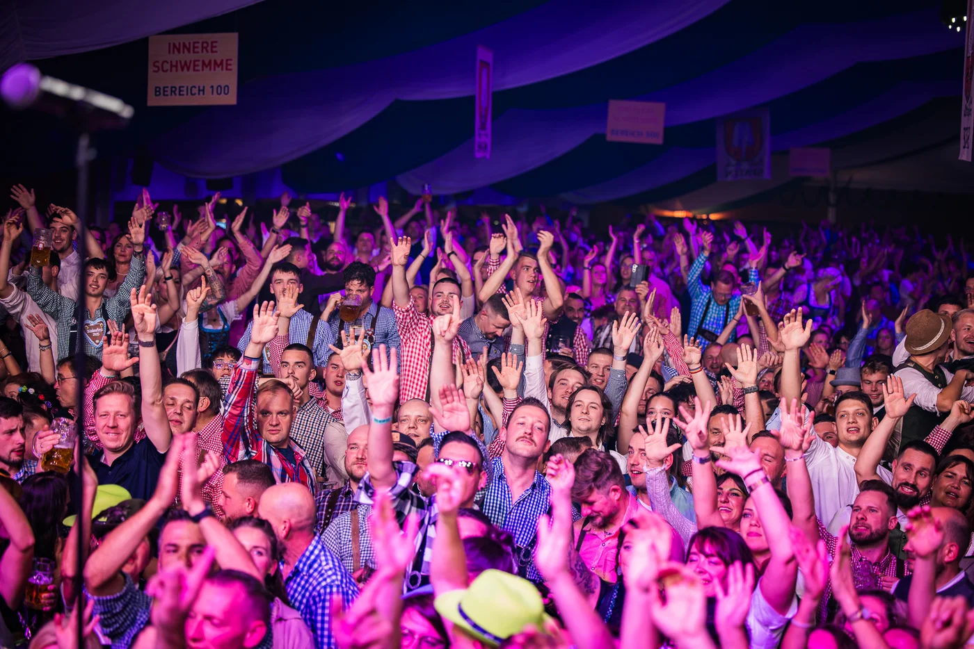 Publikum med hendene i været under lilla scenelys på Leipziger Oktoberfest.