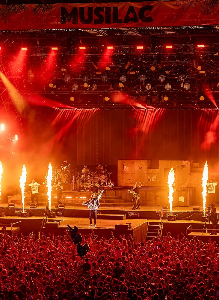 Festival Musilac: Stor scene med rødt lys, flammer og publikum.