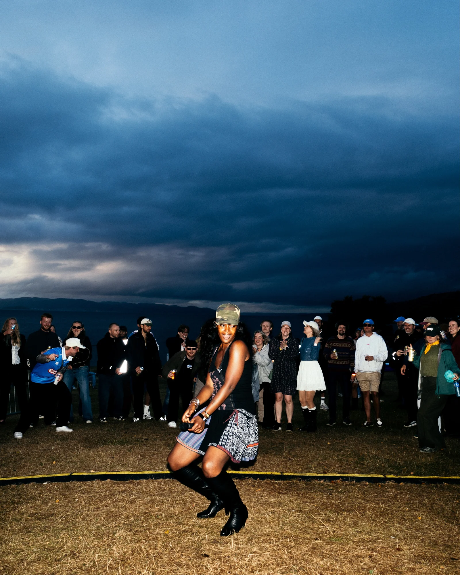 Jeløyafestivalen 2026 – dans og publikum på gresset med sjø og blå kveldshimmel i bakgrunnen